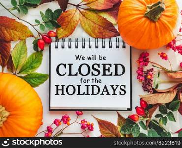 We will be closed for the Holidays. Beautiful Thanksgiving sign. Bright pumpkins, tree leaves, red berries and colorful flowers lying on an empty table. Close-up, top view. Holiday concept. We will be closed for the Holidays. Thanksgiving sign