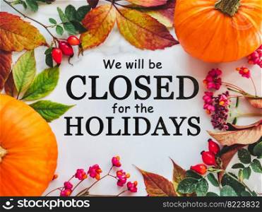 We will be closed for the Holidays. Beautiful Thanksgiving sign. Bright pumpkins, tree leaves, red berries and colorful flowers lying on an empty table. Close-up, top view. Holiday concept. We will be closed for the Holidays. Thanksgiving sign