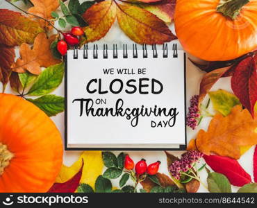 We will be closed for the Holidays. Beautiful Thanksgiving sign. Bright pumpkins, tree leaves, red berries and colorful flowers lying on an empty table. Close-up, top view. Holiday concept. We will be closed for the Holidays. Thanksgiving sign