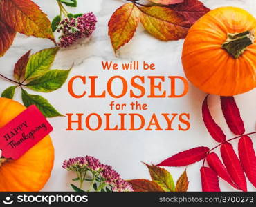 We will be closed for the Holidays. Beautiful Thanksgiving sign. Bright pumpkins, tree leaves, red berries and colorful flowers lying on an empty table. Close-up, top view. Holiday concept. We will be closed for the Holidays. Thanksgiving sign