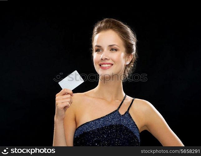 wealth, money, luxury and people concept - smiling woman in evening dress holding credit card over black background