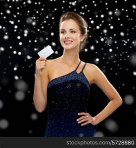 wealth, money, luxury and people concept - smiling woman in evening dress holding credit card over black snowy background