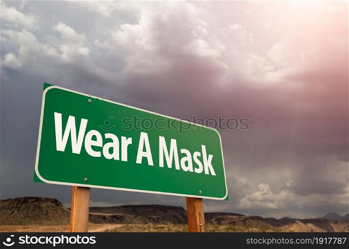 Wear A Mask Green Road Sign Against Ominous Stormy Cloudy Sky.