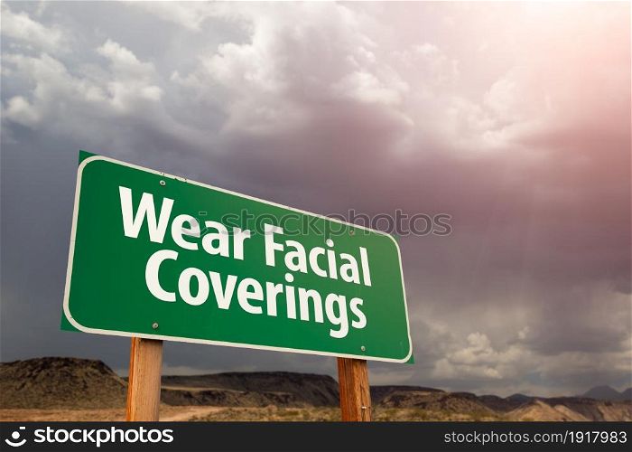 Wear Facial Coverings Green Road Sign Against Ominous Stormy Cloudy Sky.