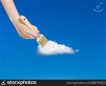 weather concept - hand with paintbrush paints solitary white cloud in blue sky in summer blue sky