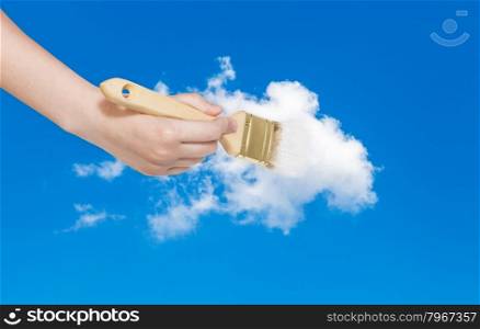 weather concept - hand with paintbrush paints white cloud in blue summer sky
