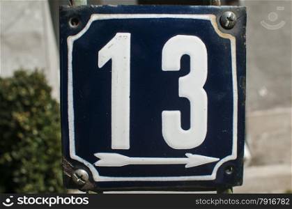 Weathered grunge square metal enameled plate of number of street address with number 13 closeup
