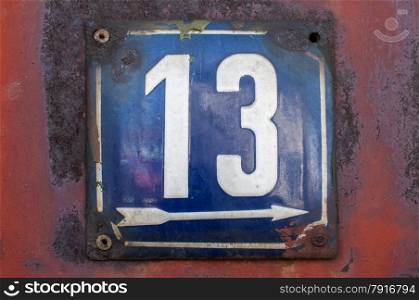 Weathered grunge square metal enameled plate of number of street address with number 13 closeup