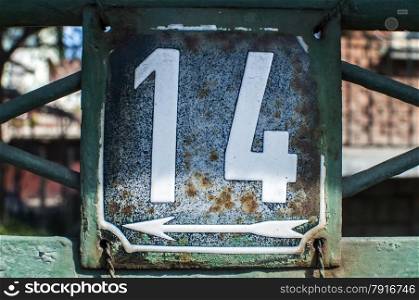 Weathered grunge square metal enameled plate of number of street address with number 14 closeup