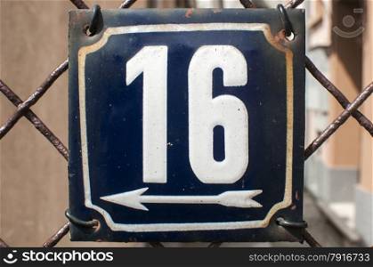 Weathered grunge square metal enameled plate of number of street address with number 16 closeup