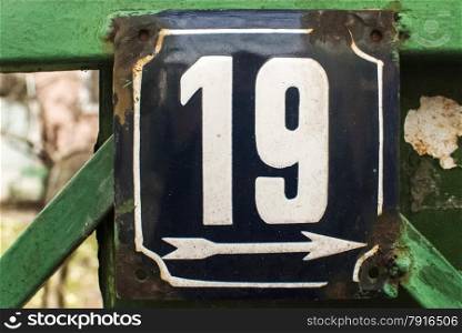 Weathered grunge square metal enameled plate of number of street address with number 19 closeup