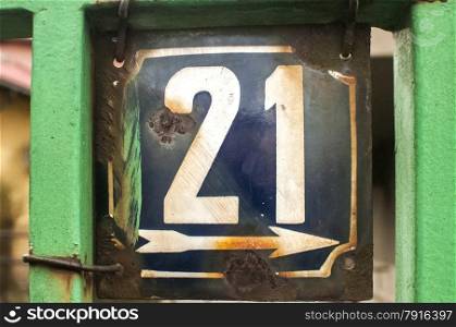 Weathered grunge square metal enameled plate of number of street address with number 21 closeup
