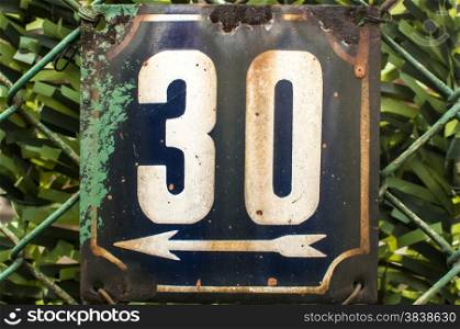 Weathered grunge square metal enameled plate of number of street address with number 30 closeup