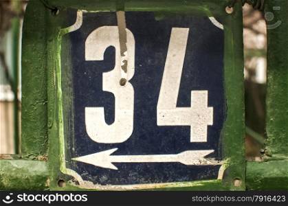 Weathered grunge square metal enameled plate of number of street address with number 34 closeup