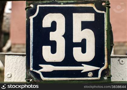 Weathered grunge square metal enameled plate of number of street address with number 35 closeup
