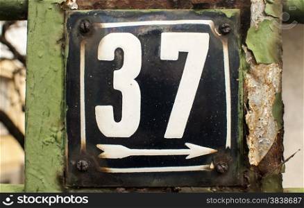 Weathered grunge square metal enameled plate of number of street address with number 37 closeup