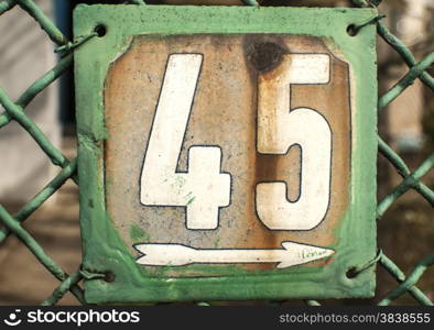 Weathered grunge square metal enameled plate of number of street address with number 45 closeup