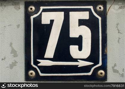 Weathered grunge square metal enameled plate of number of street address with number 75 closeup