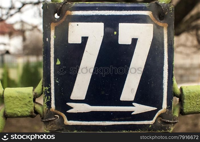 Weathered grunge square metal enameled plate of number of street address with number 77 closeup