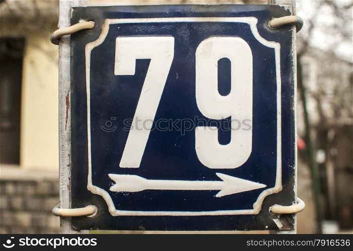 Weathered grunge square metal enameled plate of number of street address with number 79 closeup
