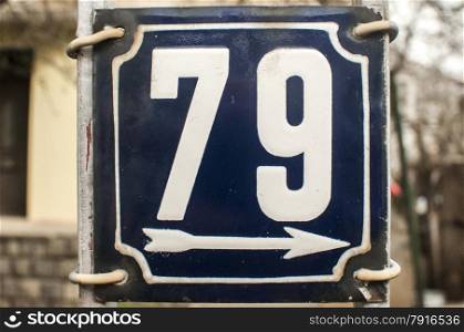Weathered grunge square metal enameled plate of number of street address with number 79 closeup