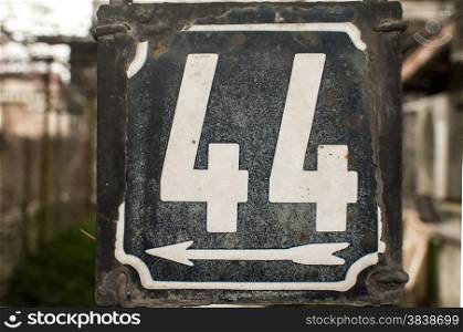 Weathered grunge square metal enamelled plate of number of street address with number 44 closeup