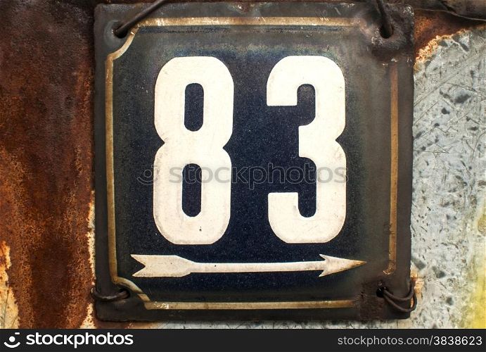 Weathered grunge square metal enamelled plate of number of street address with number 83 closeup