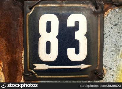 Weathered grunge square metal enamelled plate of number of street address with number 83 closeup