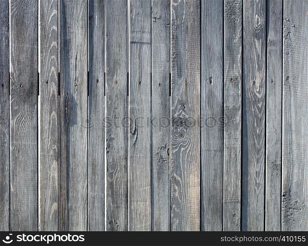 Weathered old gray wooden fence nailed with rusty nails. A weathered old gray wooden fence stands vertically