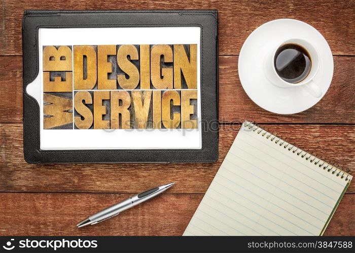 web design service word abstract in letterpress wood type on a digital tablet, top view of a rustic barn wood table with coffee and notepad