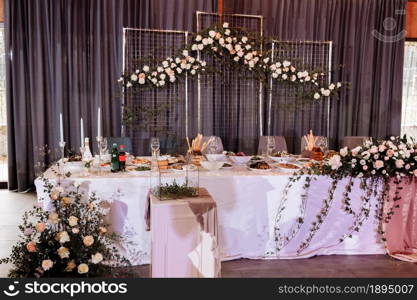 Wedding. Banquet. The festive table for bride, groom and guests, decorated with a composition of white and pink flowers and greenery, there are candles, served with crockery in restorane.. Wedding. Banquet. The festive table for bride, groom and guests, decorated with a composition of white and pink flowers and greenery, there are candles, served with crockery in restorane