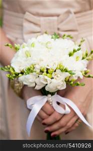 Wedding bouquet from white freesias closeup in bride&rsquo;s hands