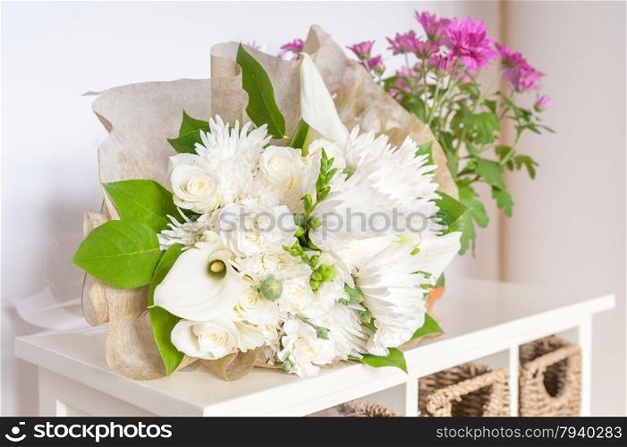 wedding bouquet of white flowers and green foliage with pink flowers in the background