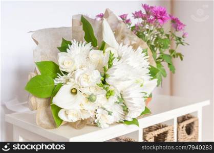 wedding bouquet of white flowers and green foliage with pink flowers in the background