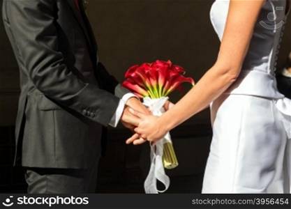 wedding bouquet. the hands of the newlyweds are intertwined touch of a bouquet of red flowers