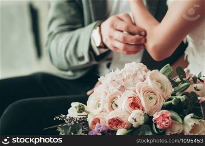 Wedding bouquet with blurred bride and groom in the background, holding each other hands