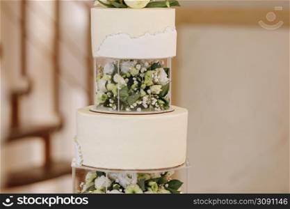 Wedding cake. Close-up photo of a beautiful white three-tiered wedding cake decorated by flowers and greenery.. Wedding cake. Close-up photo of a beautiful white three-tiered wedding cake decorated by flowers and greenery