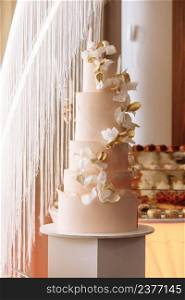 Wedding cake. Close-up photo of a festive beautiful pink five-tiered wedding cake decorated by white and gold flowers. candy bar.. Wedding cake. Close-up photo of a festive beautiful pink five-tiered wedding cake decorated by white and gold flowers. candy bar