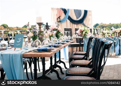 Wedding catered event setting, flowers, candles, white plates, blue napkins, wooden tables, Event decoration, outdoors, sunny summer day