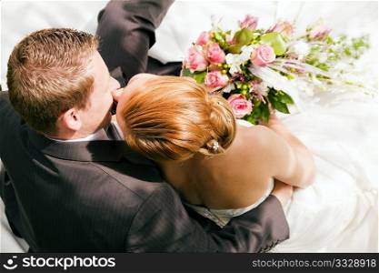 wedding couple hugging and kissing, the bride holding a bouquet of flowers in her hand