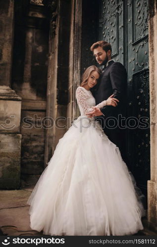 Wedding couple hugs near the vintage green door. Stone walls in ancient town background. bride with long hair in lace dress and groom in suit and bow tie. Tender embrace. Romantic love. Wedding couple hugs near the vintage green door. Stone walls in ancient town background. bride with long hair in lace dress and groom in suit and bow tie. Tender embrace. Romantic love.