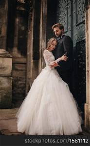 Wedding couple hugs near the vintage green door. Stone walls in ancient town background. bride with long hair in lace dress and groom in suit and bow tie. Tender embrace. Romantic love. Wedding couple hugs near the vintage green door. Stone walls in ancient town background. bride with long hair in lace dress and groom in suit and bow tie. Tender embrace. Romantic love.