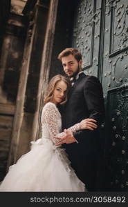 Wedding couple hugs near the vintage green door. Stone walls in ancient town background. bride with long hair in lace dress and groom in suit and bow tie. Tender embrace. Romantic love. Wedding couple hugs near the vintage green door. Stone walls in ancient town background. bride with long hair in lace dress and groom in suit and bow tie. Tender embrace. Romantic love.