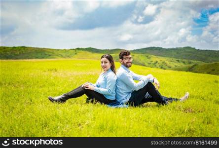 Wedding couple in the field sitting back to back facing the camera, A wedding couple sitting back to back on the grass