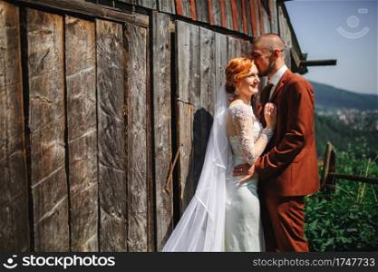 Wedding couple in the mountains. The groom and bride are hugging near the rustic house. A beautiful view of the mountains behind the couple.. Wedding couple in the mountains. The groom and bride are hugging near the rustic house. A beautiful view of the mountains behind the couple