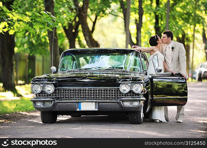 Wedding couple kissing near car after their wedding ceremony