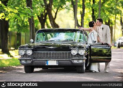 Wedding couple kissing near car after their wedding ceremony