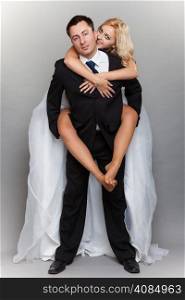 Wedding day. Cheerful married couple having fun piggyback riding young smiling people embracing, love and affection studio shot, gray background