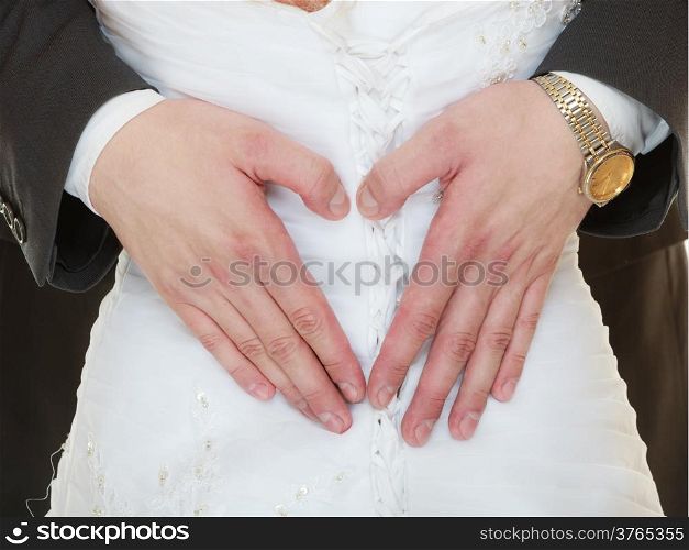 Wedding day. Closeup of male hands on back of bride in white dress. Man groom showing making heart shape love symbol. Studio shot.