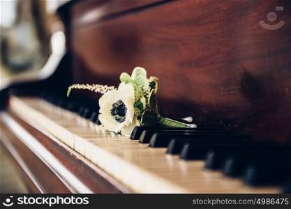 Wedding day concept. Boutonniere flower for groom on the vintage piano keys.